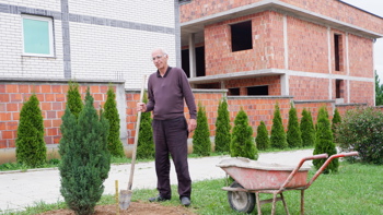 A man plants a tree outside of a house in Arllat village in Kosovo