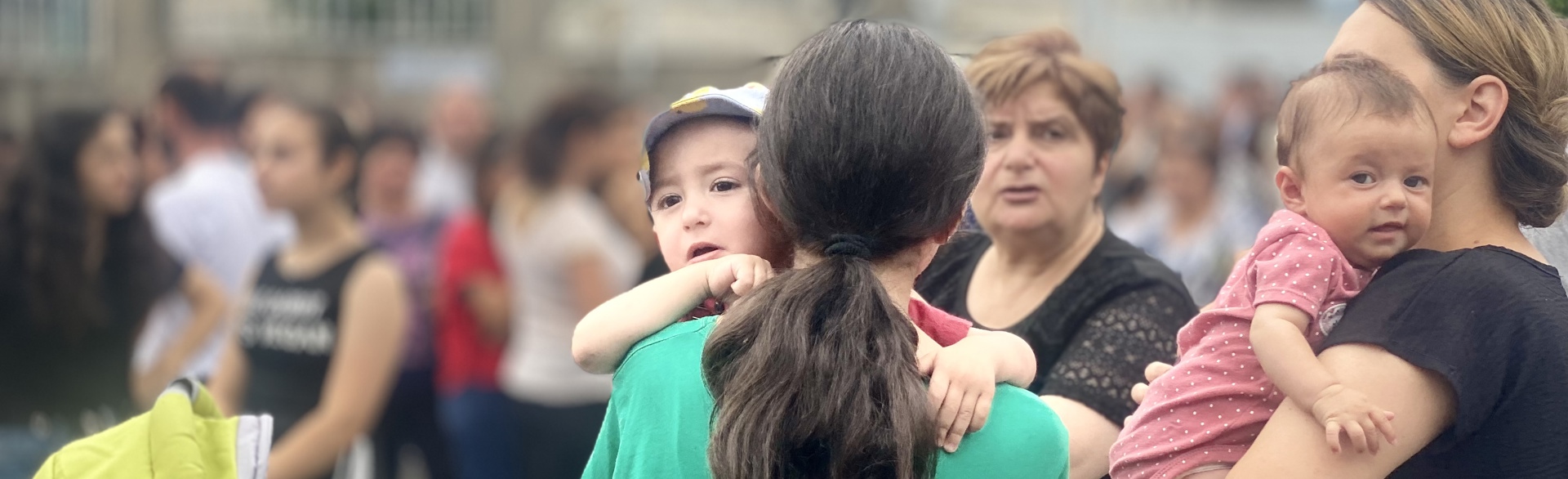 Mothers hold their babies amongst a crowd of people outside