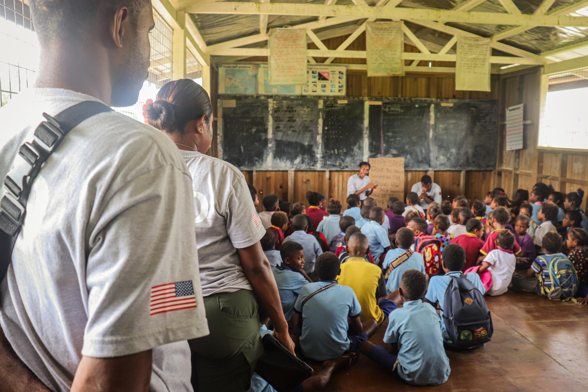 HALO staff watch from the back of a classroom while a large group of school children participate in a risk education lesson.