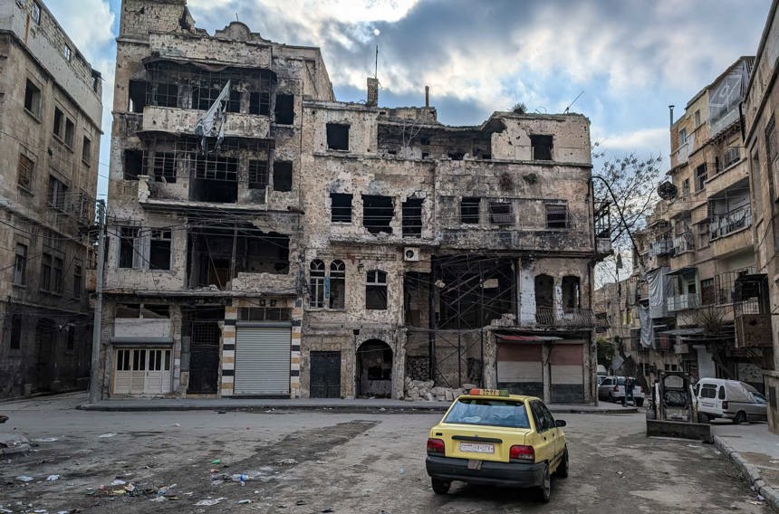 A taxi sits in front of a destroyed building in Central Aleppo
