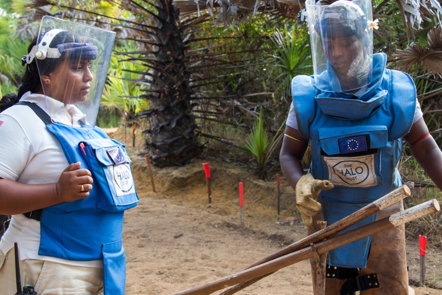Two deminers hold vegetation cutting tools in Sri Lanka whilst wearing personal protective equipment and visors