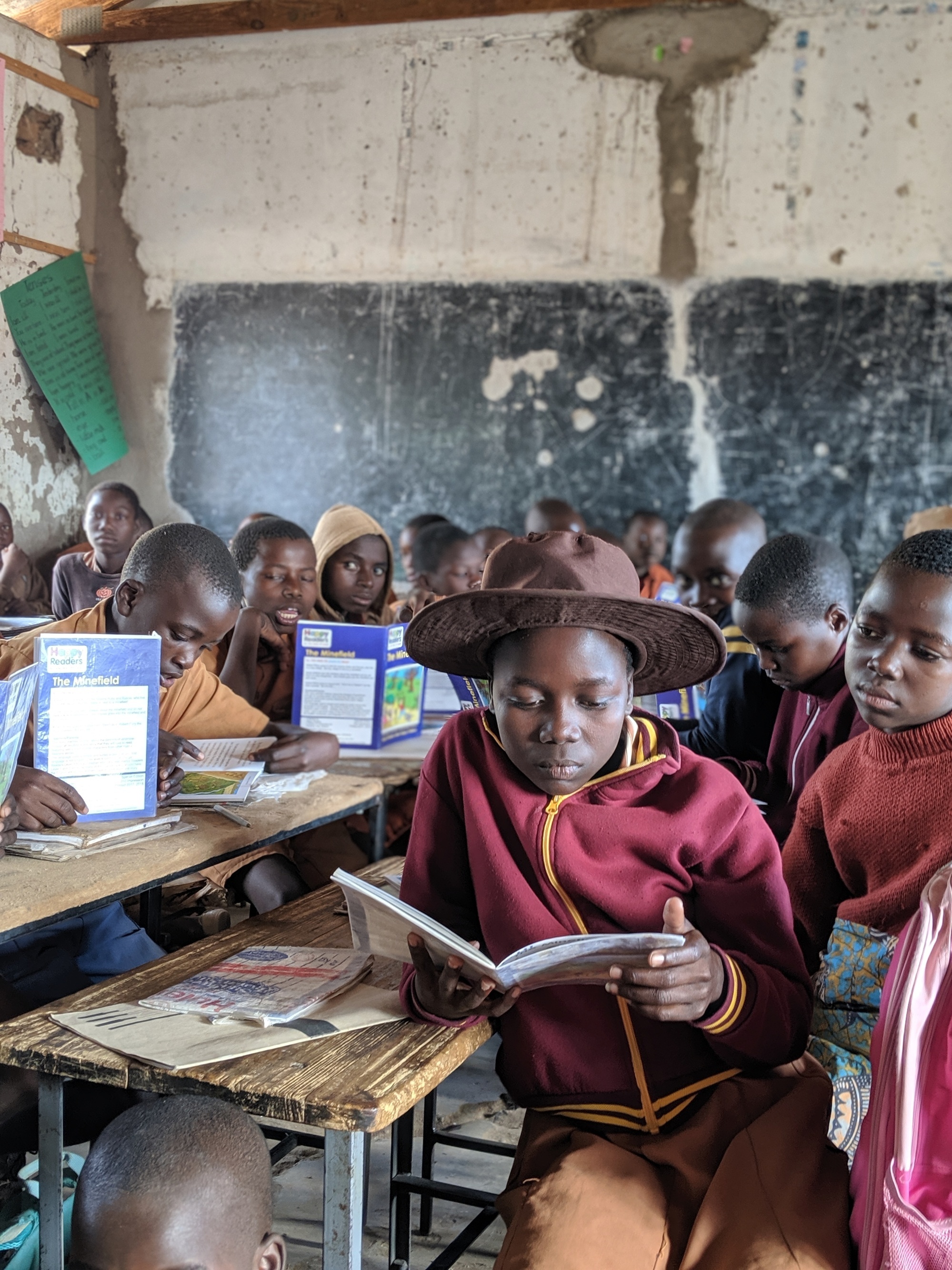 A group of schoolchildren sit at tables in a classroom reading safety books about minefields