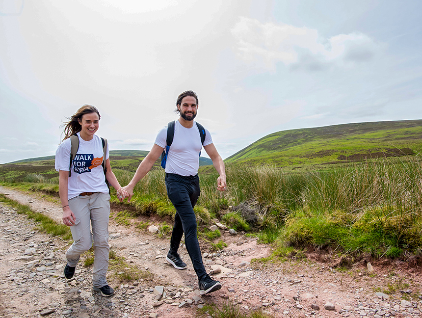 Camilla Thurlow and Jamie Hewitt walk hand in hand on a grassy track during the Safe Steps for Syria fundraising walk