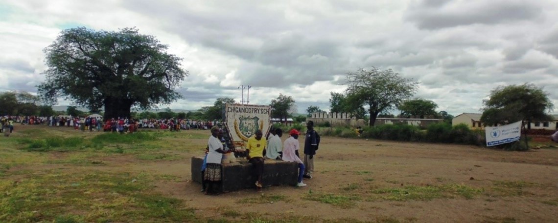 Crowds gather at Chigango Primary School, opposite the road from the windmill, to collect food aid from WFP, HALO Trust.