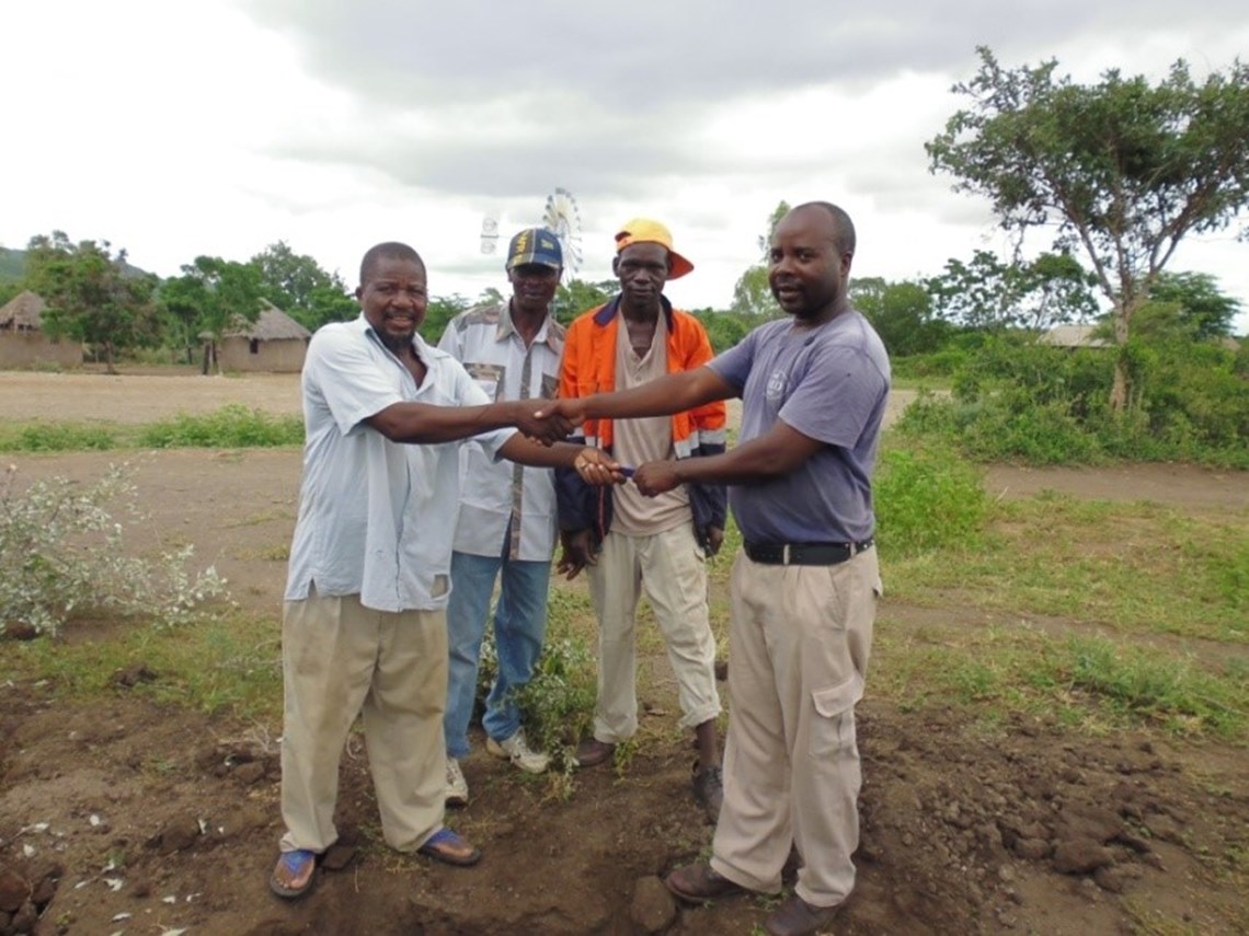 Demining Manager July and Bandimba (back right) hand over responsibility for the gate valve to the village elders, HALO Trust.