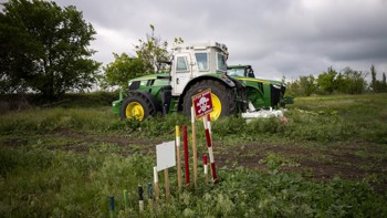 A large agricultural machine stands in the middle of a field behind a landmine warning sign.