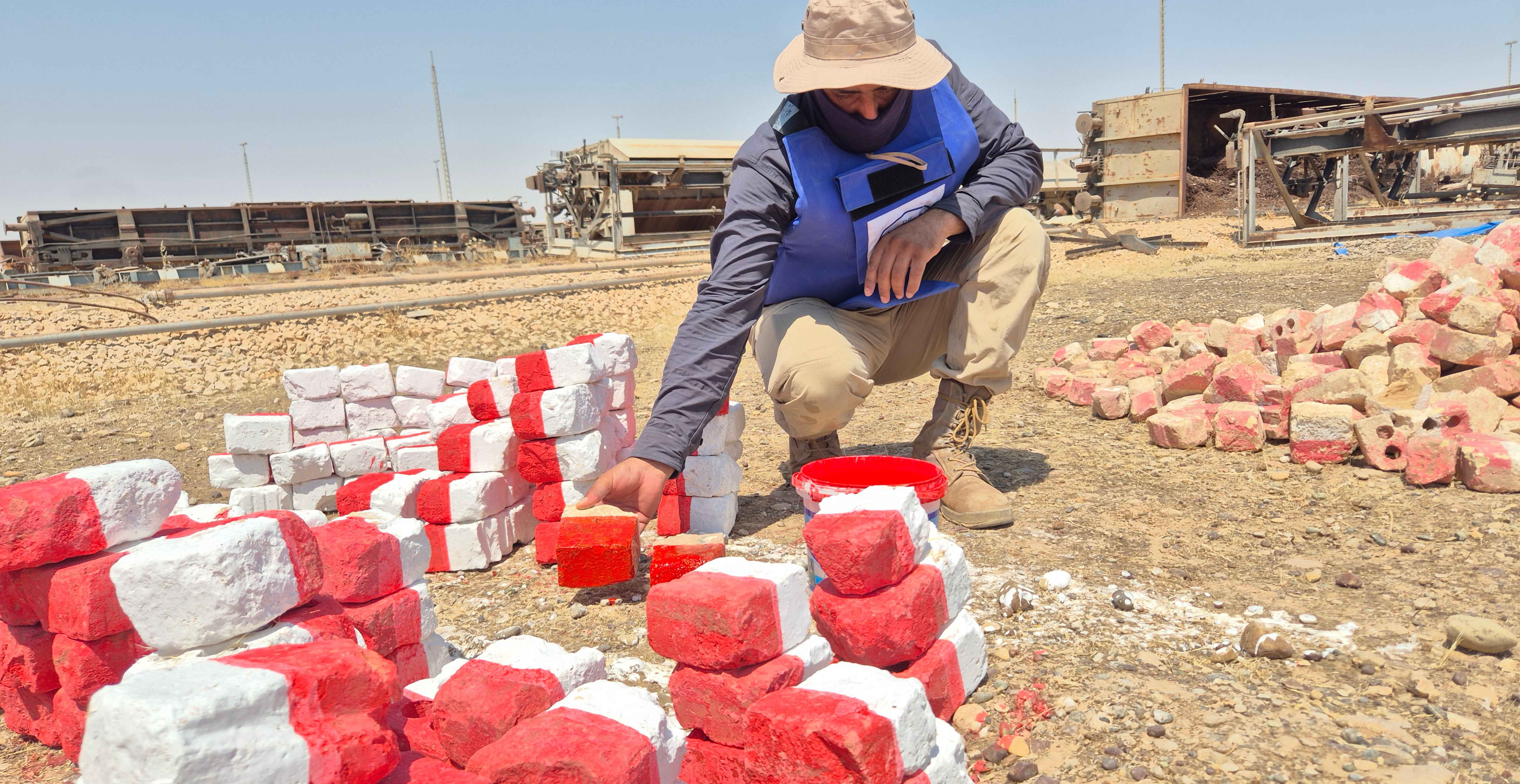 A HALO deminer in Baiji, Iraq with piles of red and white stones marking 'danger'.