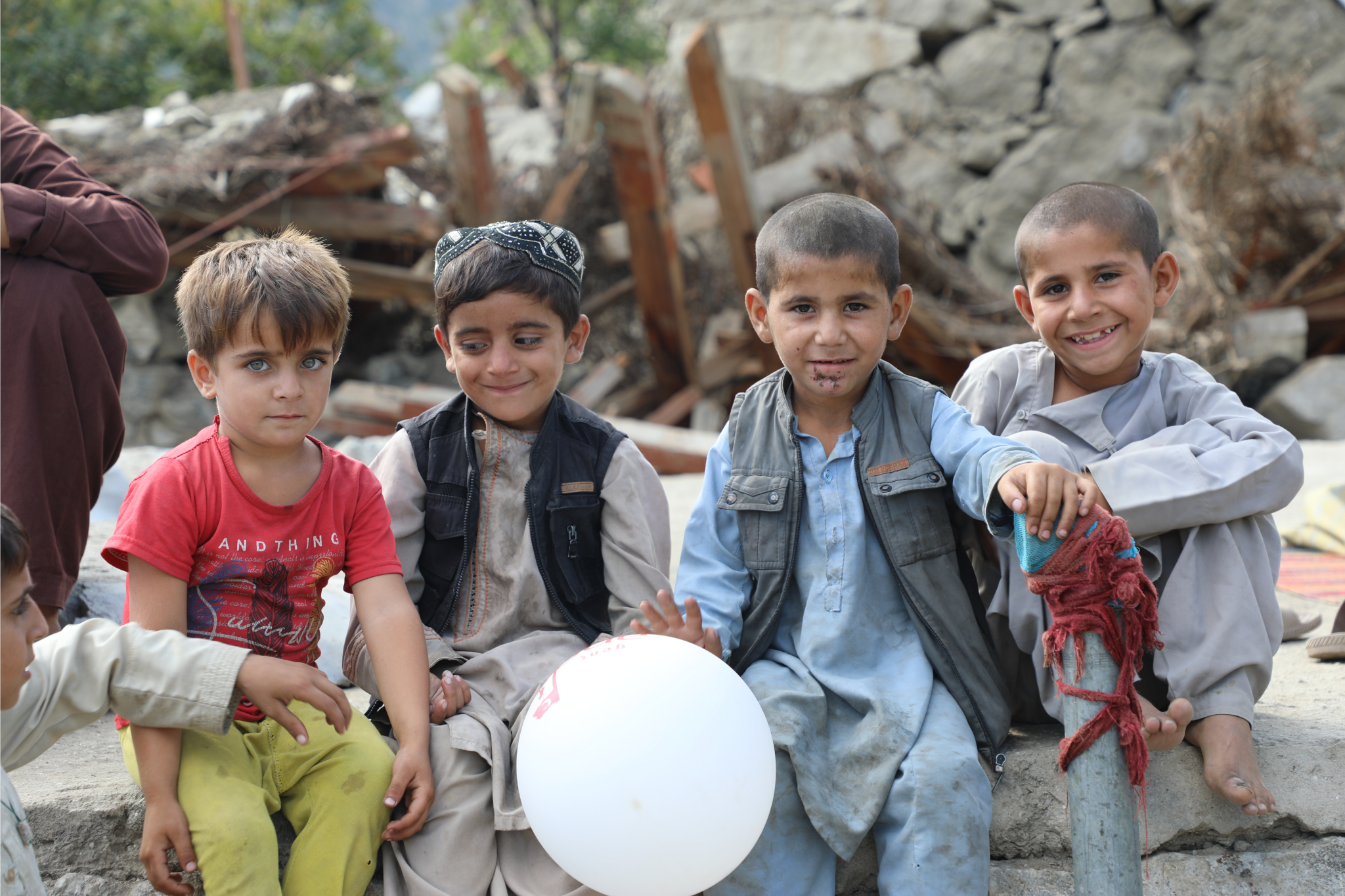 Four children sit and smile with a ballon on top of earthquake rubble.