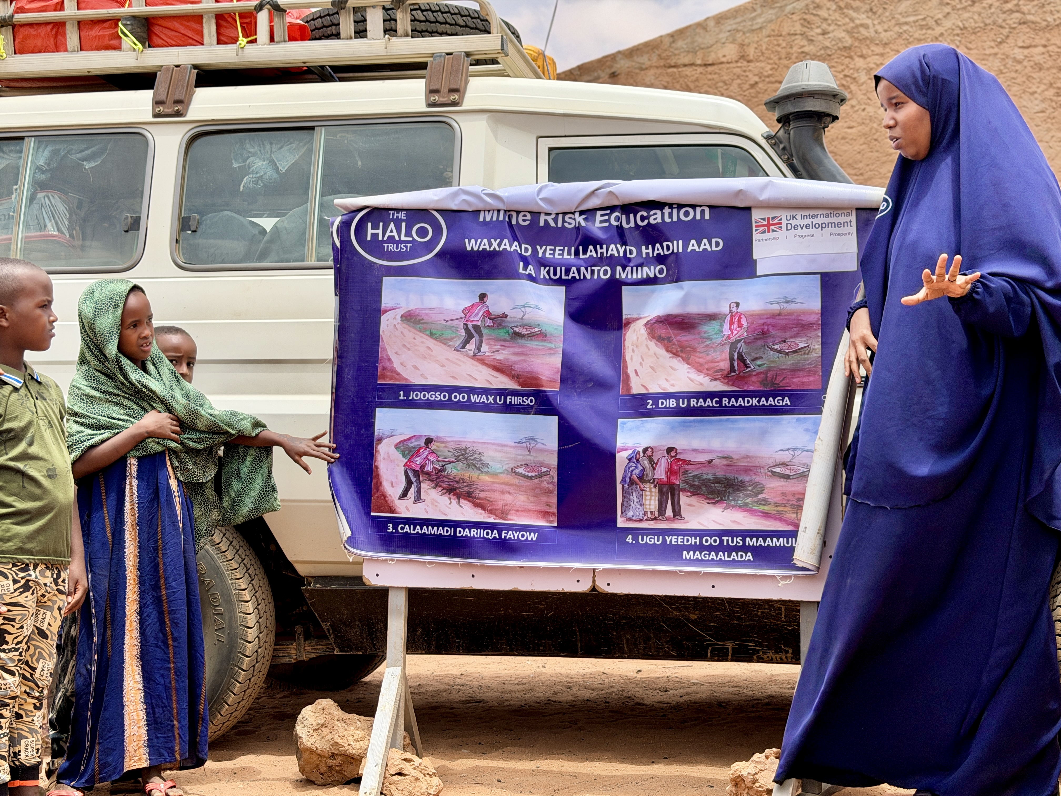 A woman teaches safety to a group of children in Somalia using boards displaying photographs
