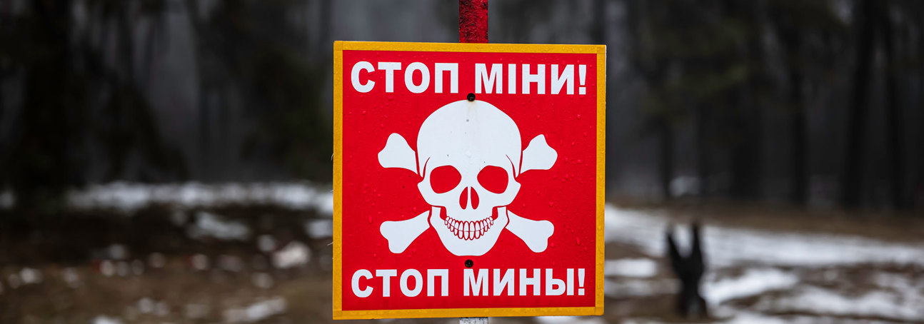 A red danger mines sign with a skull and crossbones and message in Ukrainian standing in a snow covered minefield