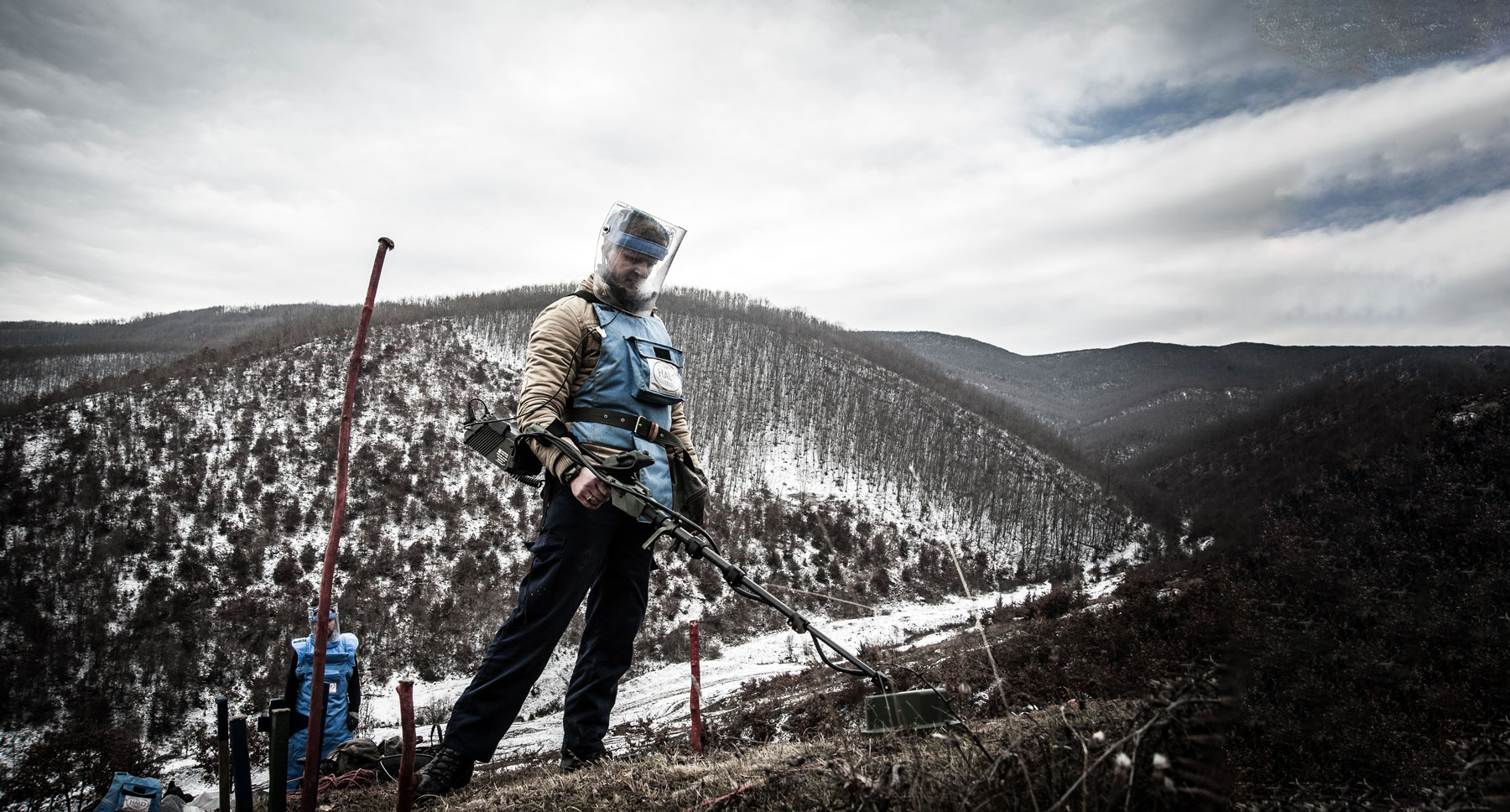 A deminer in Kosovo holds a detector whilst standing on a snow covered hill