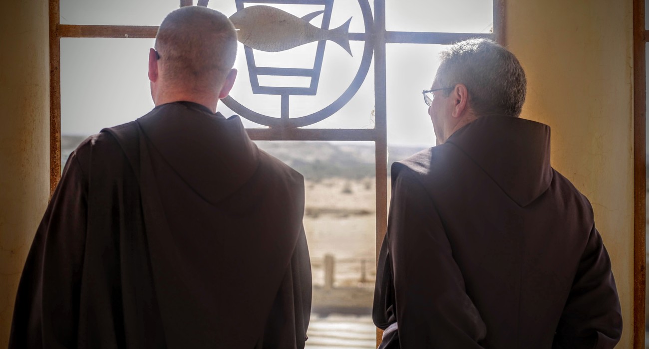 The head of the Franciscan Mission and a HALO Trust staff member stand and look out of the window of the recently cleared compound