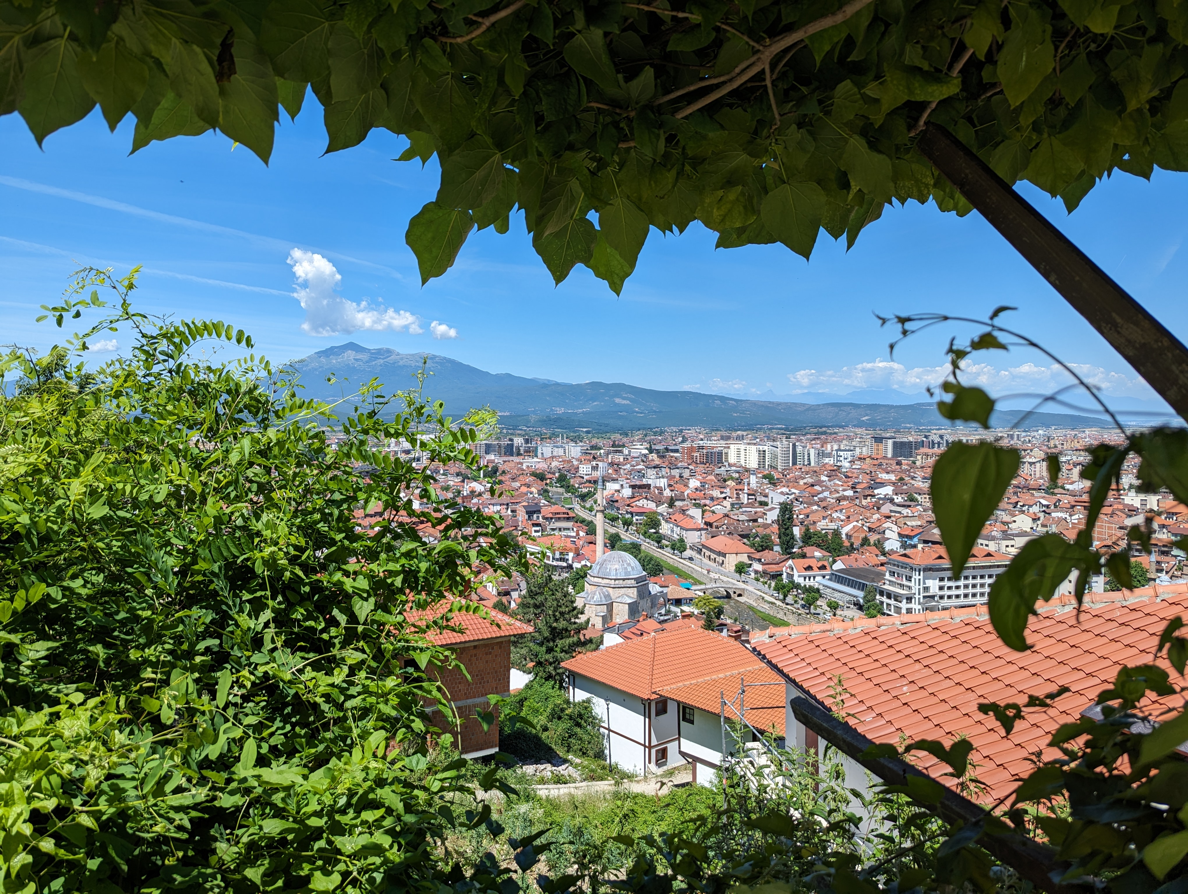 Rooftops over a thriving Kosovan neighbourhood with blue skies and mountains in the background