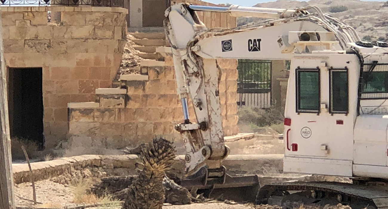 A armoured digger conducts clearance and removal of explosives from the contaminated Franciscan Compound