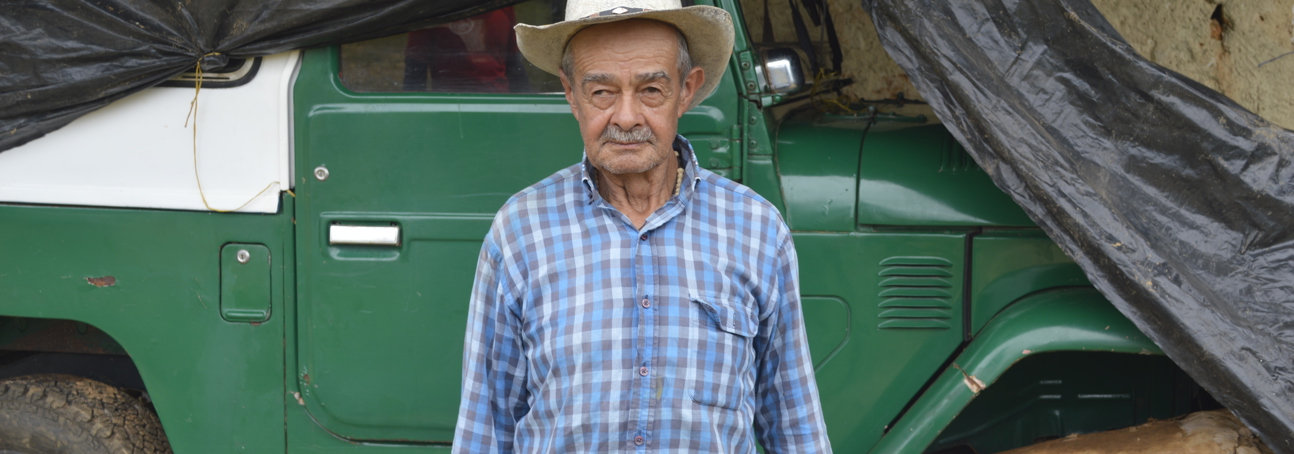 A Colombian farmer stands in front of a large jeep like vehicle
