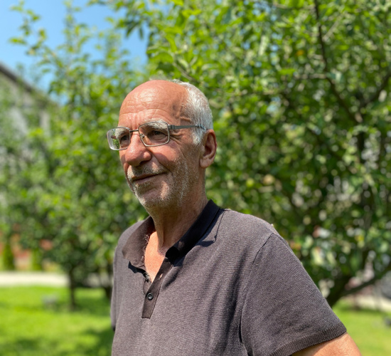 Maliq, a local resident from Arllat, stands in his garden in front of an apple tree