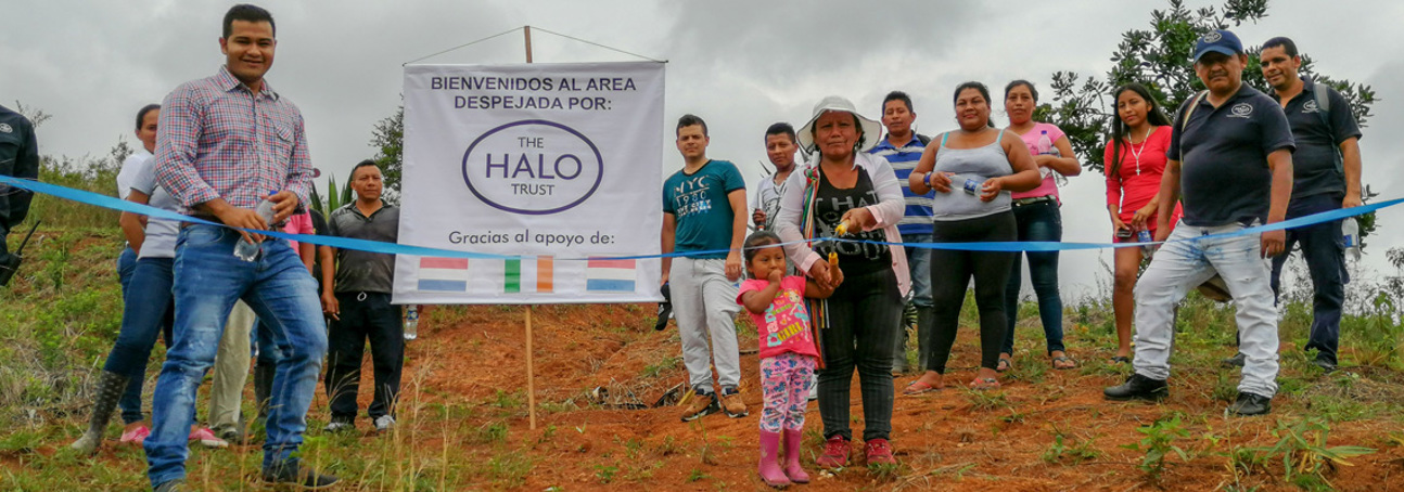 Staff and locals in Colombia cut a ribbon to celebrate a land handover from HALO. A poster behind them also thanks HALO's donors.