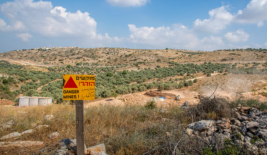 A landmine warning sign is planted before the hills and rural land of the West Bank