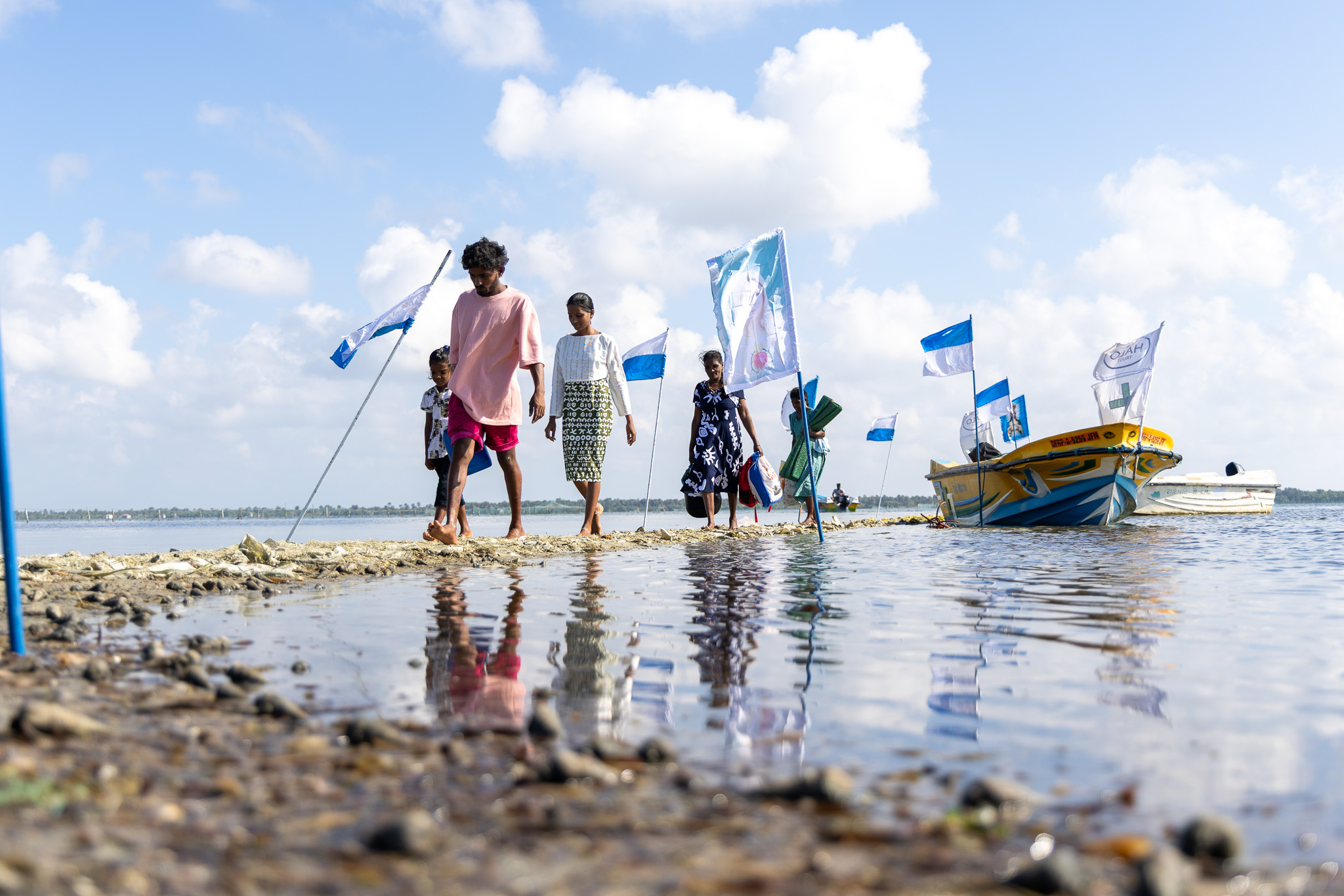 Five people walk on a small isle off their boat, their figures are reflected in the lagoon.