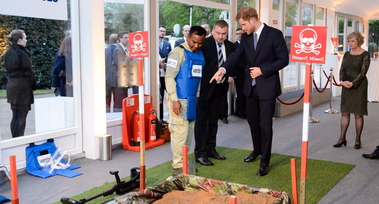 Prince Harry talks with a HALO Trust staff member wearing a protective vest near a display minefield at an event