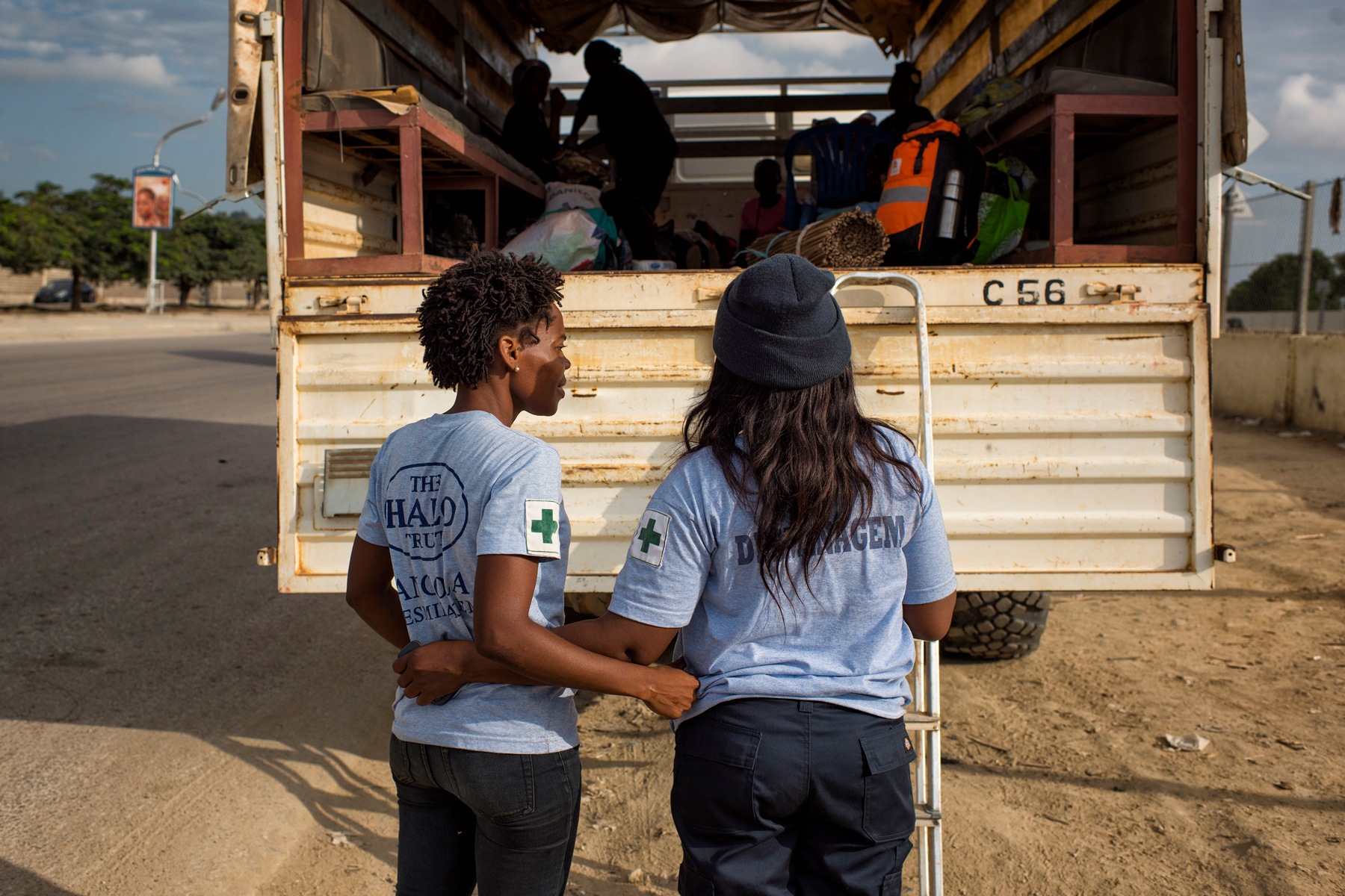 Two female deminers stand at the back of a large vehicle wearing HALO tshirts