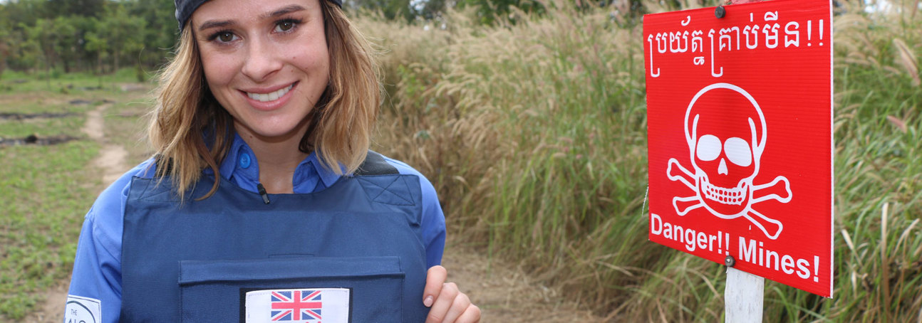 Camilla Thurlow stands in PPE in front of a Danger Mines sign in a field in Cambodia during her training