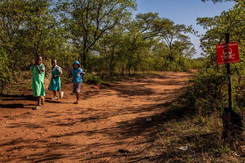 Children walk on a sandy track next to a danger mines sign