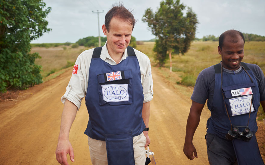 James Cowan, the HALO Trust CEO walks on a sandy track wearing PPE