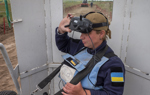 A woman in a HALO Trust vest operates a large remote control and looks into a pair of goggles.