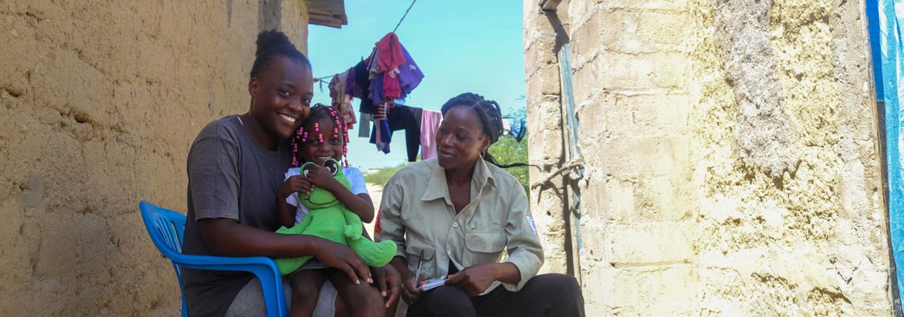 A woman and child sit next to a HALO staff member outside their home in Angola