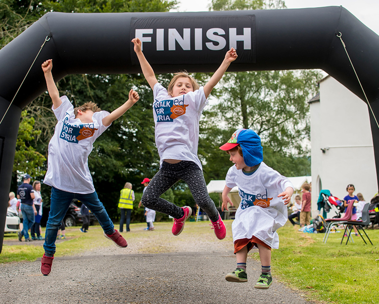 Kids jump in celebration at the finish line as they reach the end of their walk for Syria