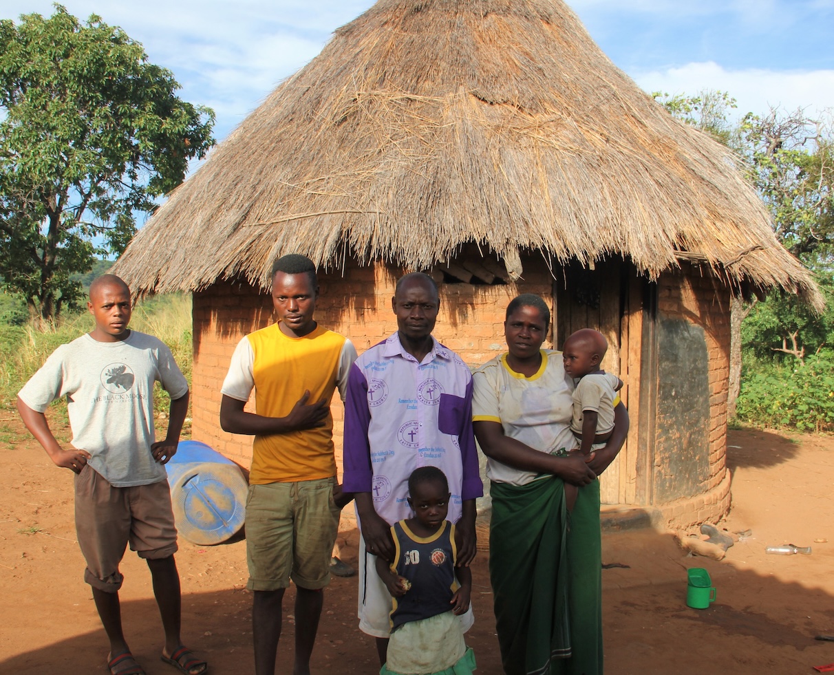 Miriam poses with their family outside a hut