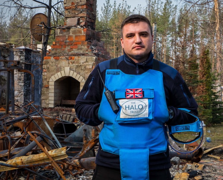 Denys, a minefield supervisor stands in front of a collapsed house