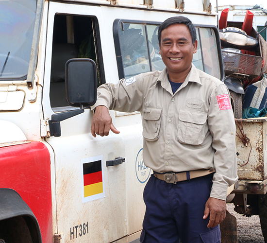 Mr Houn Ny stands next to a vehicle while wearing HALO uniform