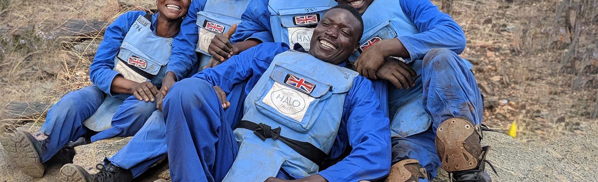 A team of UK-funded deminers sit and pose whilst laughing for a photo on their break