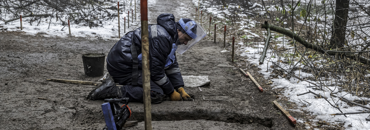 A deminer excavates the soil whiles wearing PPE in a snowy mine marked area