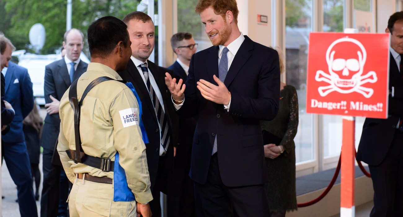 Prince Harry talks with a HALO Trust staff member wearing a protective vest near a display minefield at an event