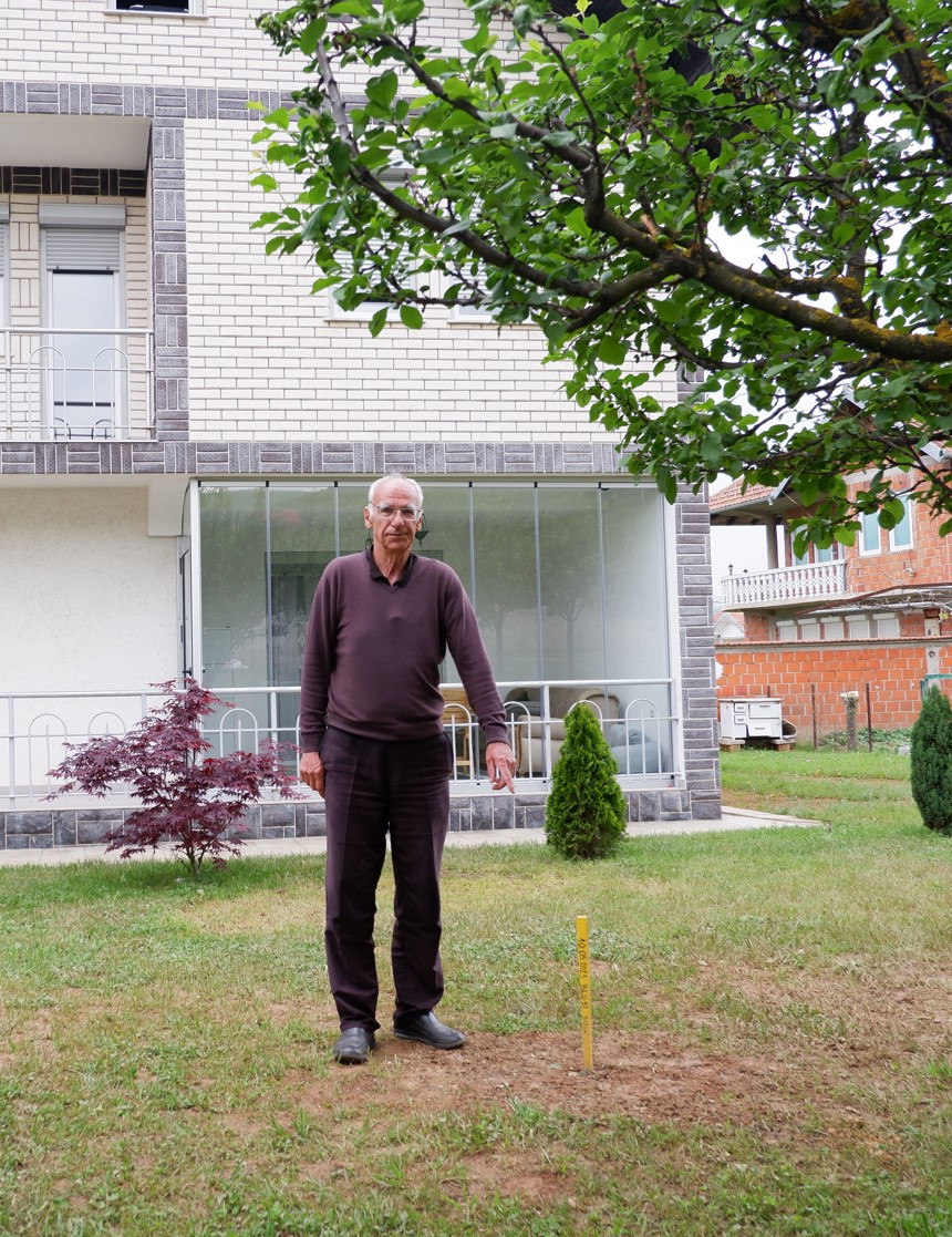 Maliq stands in his garden pointing to a stick where a cluster munition was found