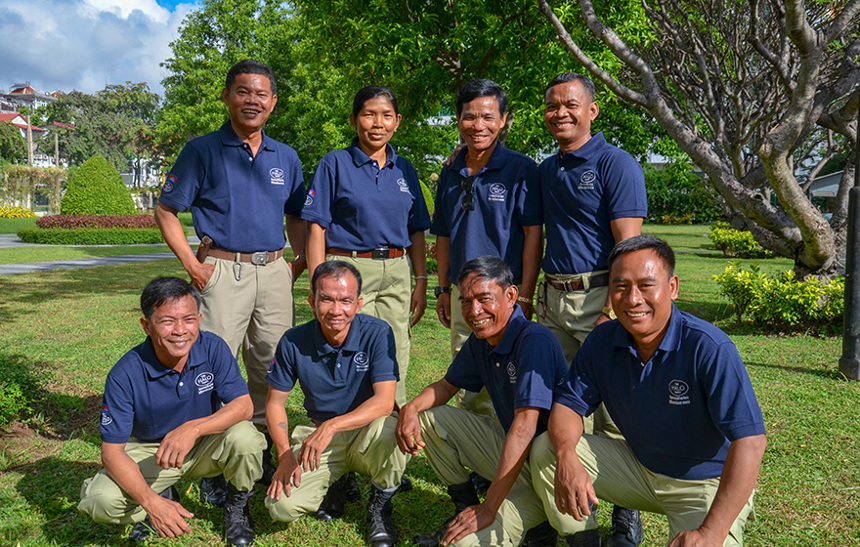 A group of eight deminers stand in uniform in a garden in Cambodia
