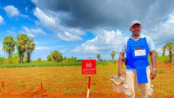 Balamuralee Balasingam stands in front of a Danger Mines sign in a minefield in Sri Lanka