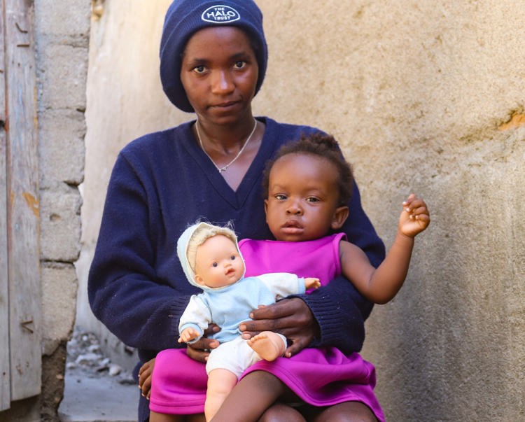 HALO worker, Rebeca Cupenala, sits with her daughter on her lap whilst holding a doll