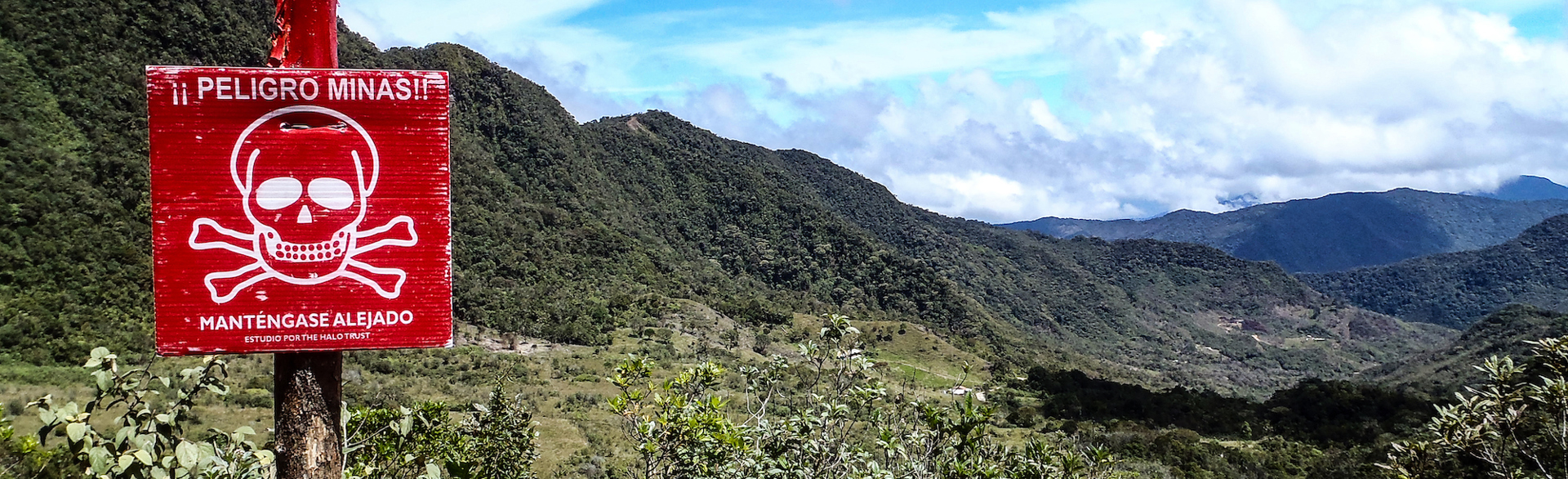A scenic view of valleys, forests, and hills in Colombia with a mine warning sign in the foreground
