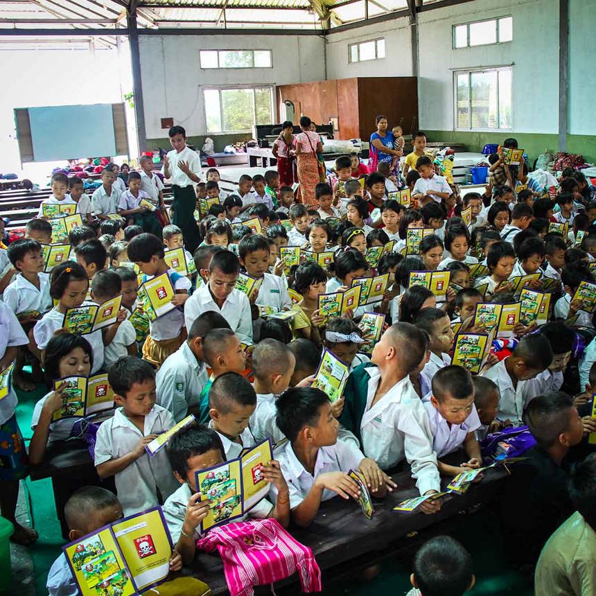 Several dozen children holding mine risk education booklets in Myanmar.