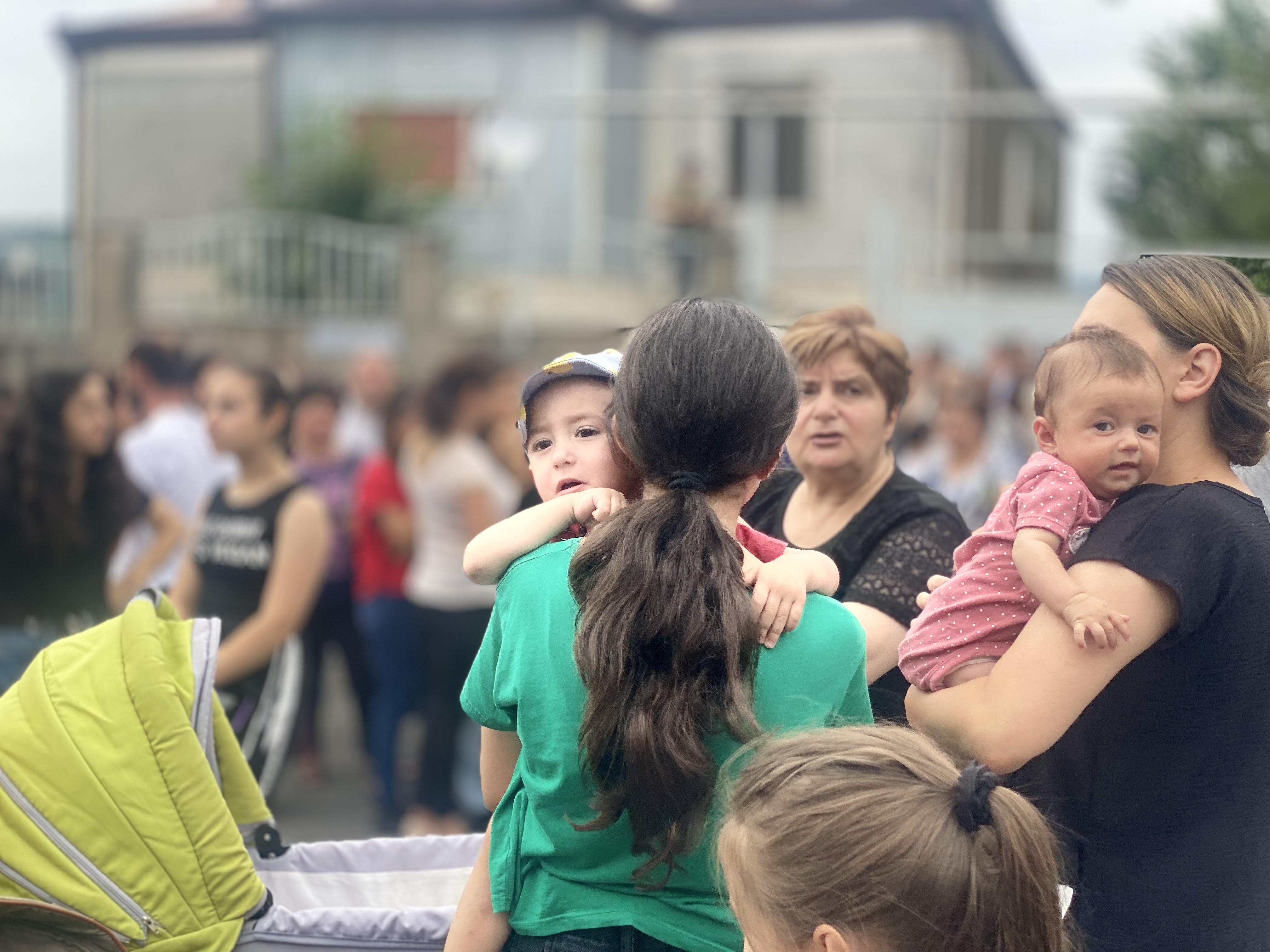 Mothers hold their babies amongst a crowd of people outside