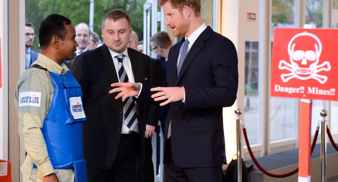 Prince Harry talks with a HALO Trust staff member wearing a protective vest near a display minefield at an event