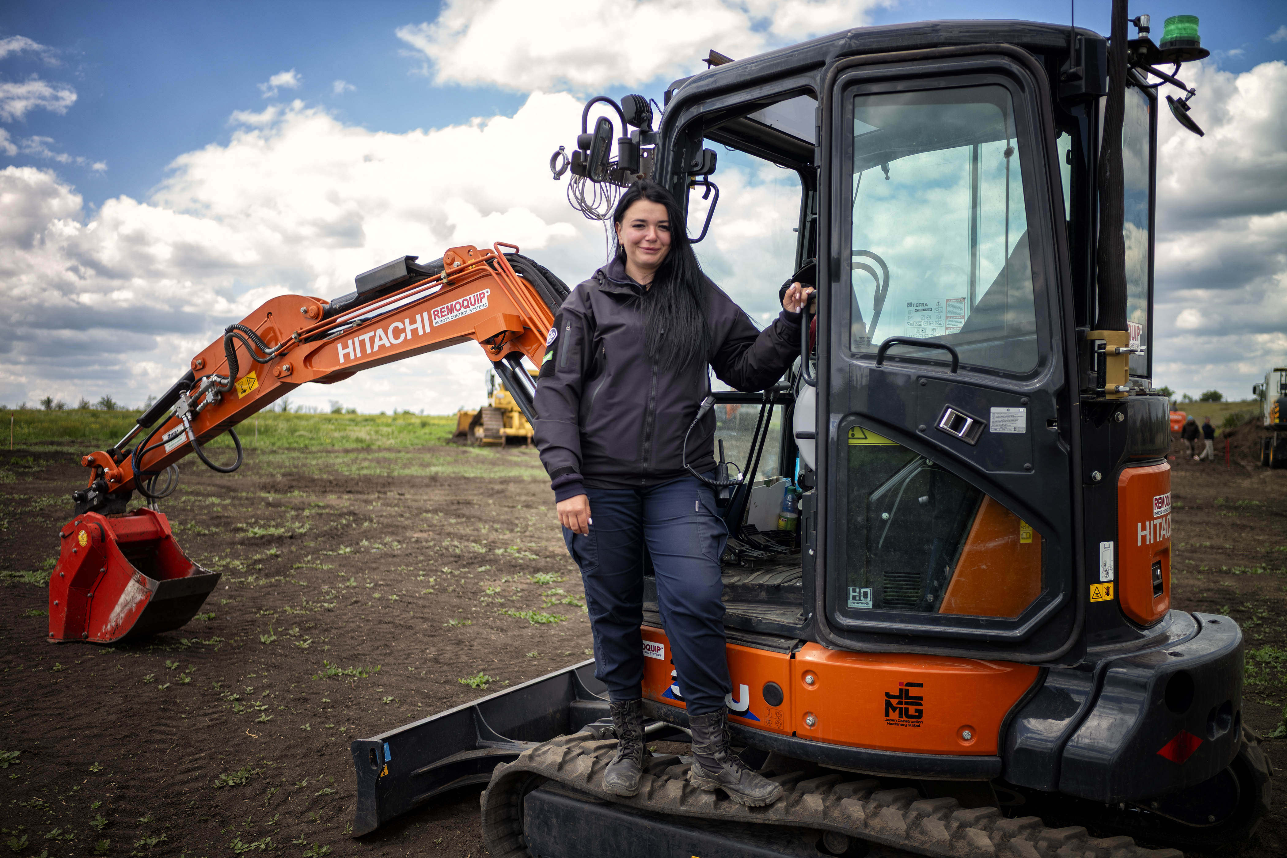 A woman stands on a mini excavator