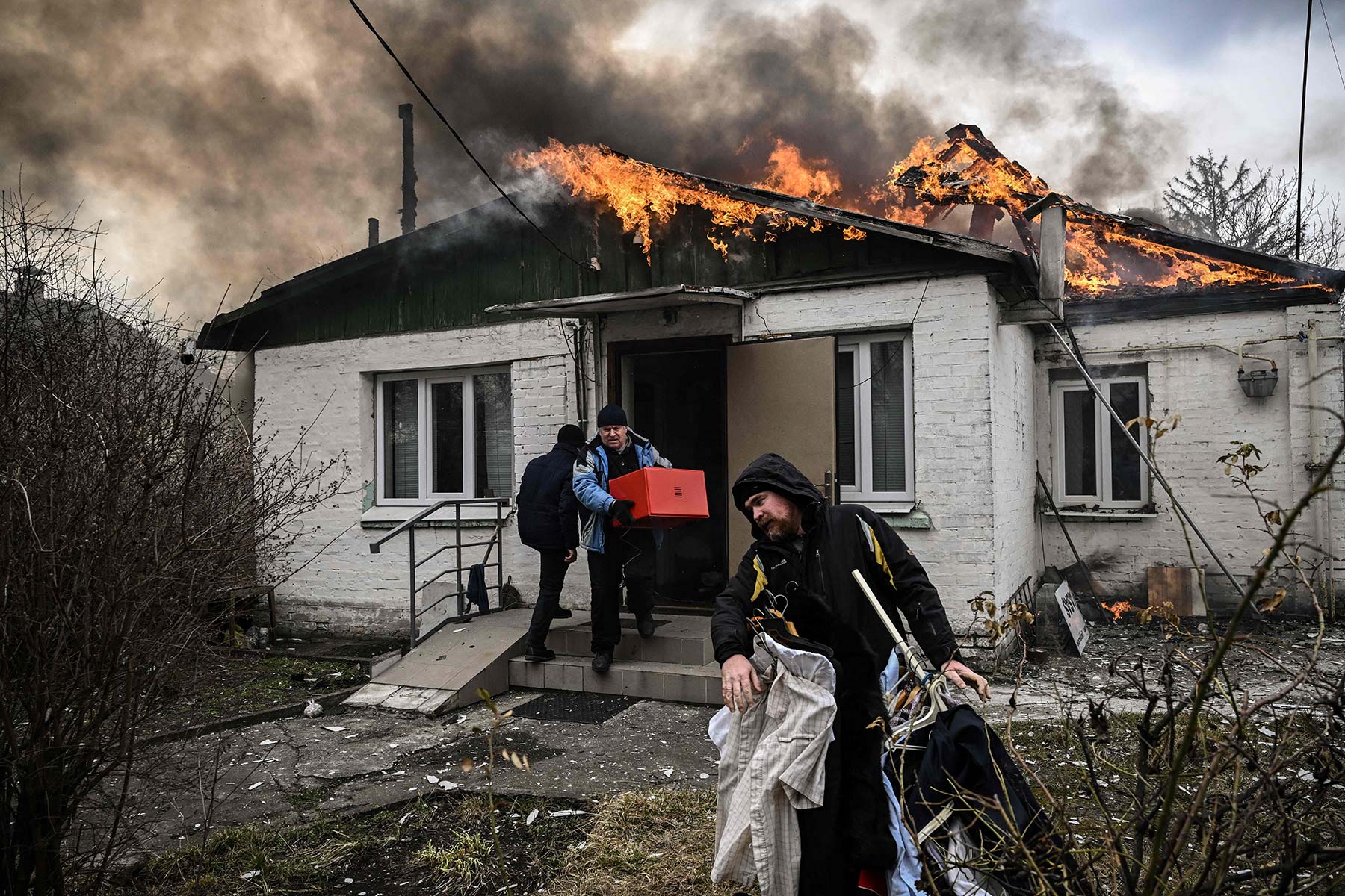 Three men work to get belongings out of a home that has its roof on fire