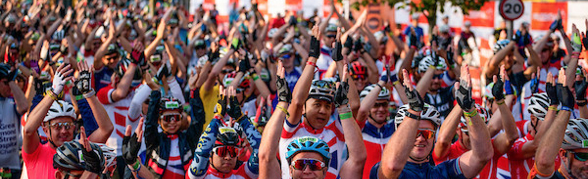 A crowd of cyclists clap and raise their hands at the finish line