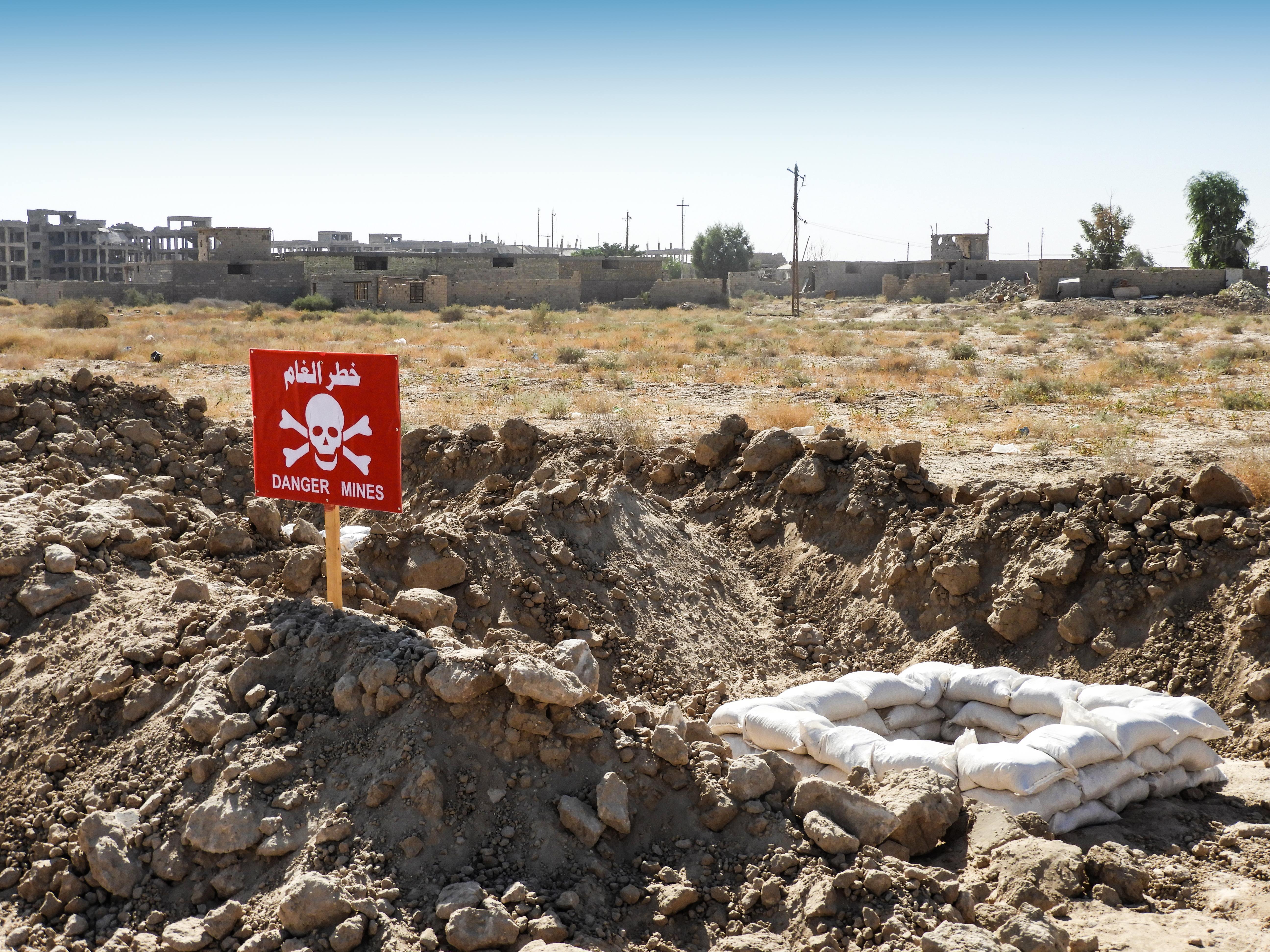 Mine warning sign with sandbags and destroyed buildings in the background 