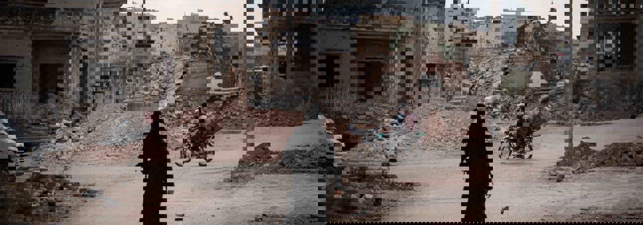 Woman dressed in black, walking through a street in Syria surrounded by rubble from destroyed buildings